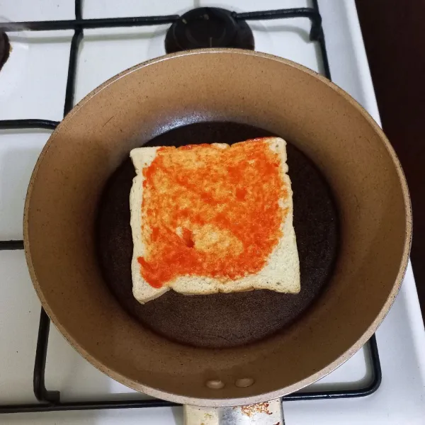 Panaskan teflon tata roti tawar di atasnya, tambahkan saus pedas lalu ratakan.