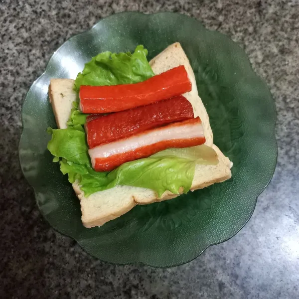 Siapkan roti tawar, tata daun selada dan letakkan crabstick di atasnya.