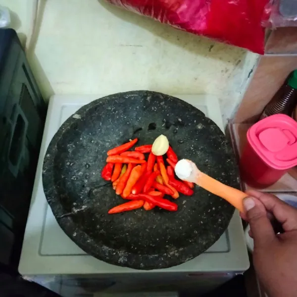 Membuat sambal penyet : siapkan cobek, kemudian masukkan cabai rawit merah dan bawang putih, lalu beri garam, kaldu bubuk dan sedikit gula pasir.