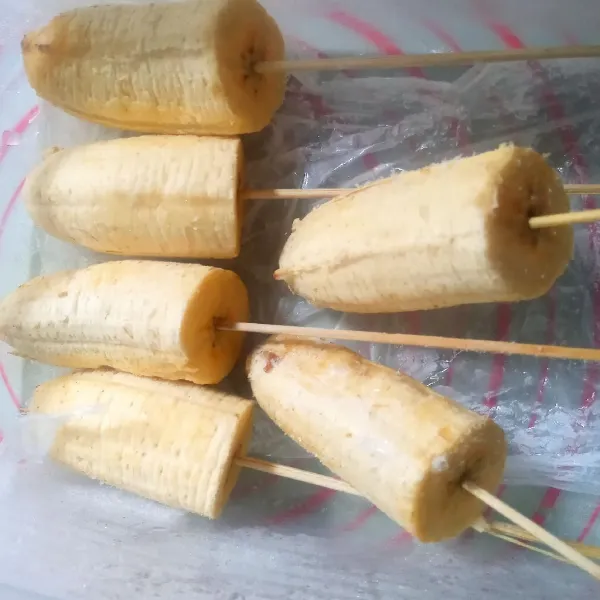 Potong pisang yang sudah dikupas menjadi dua bagian. Tusuk menggunakan tusuk sate kemudian bekukan dalam freezer minimal selama 1 malam.