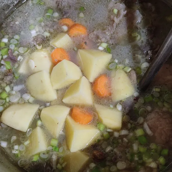 Masukkan bumbu ke kuah tulang, aduk rata, masukkan wortel dan kentang serta garam.
