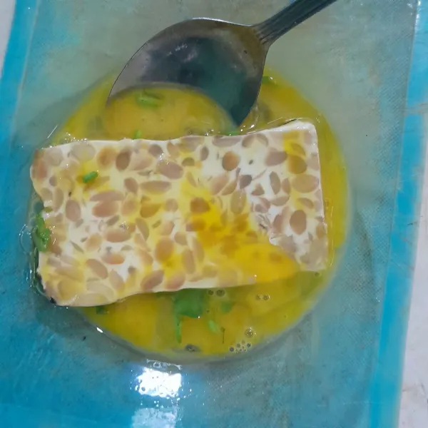 Masukkan tempe ke dalam telur, baluri tempe dengan telur.