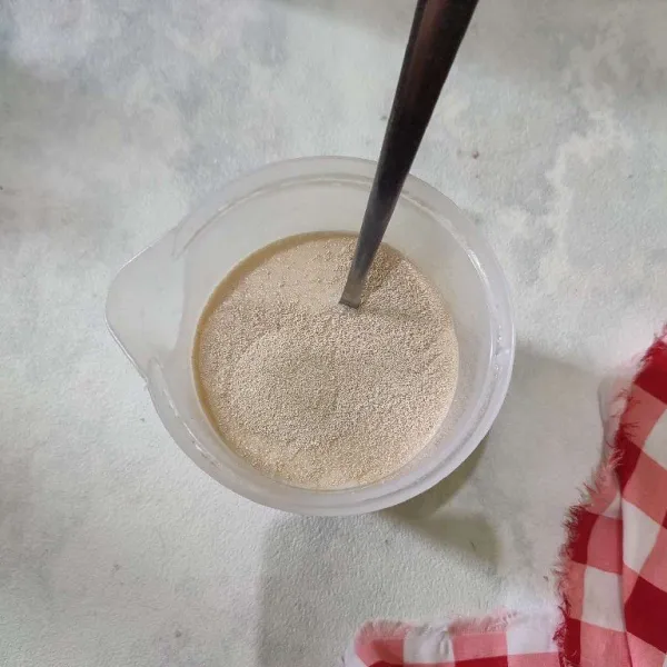 Campurkan ragi dengan gula pasir dan susu hangat, aduk rata.