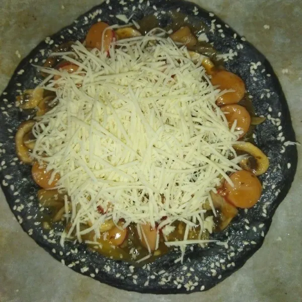Oles bagian dough pizza dengan sedikit air, lalu taburi wijen secukupnya, lalu taburi pizza dengan keju parut.