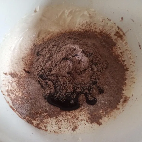 Selanjutnya masukkan tepung terigu, baking powder, cokelat bubuk dan vanili sambil diayak. Tambahkan juga kental manis kemudian kocok sebentar asal rata.