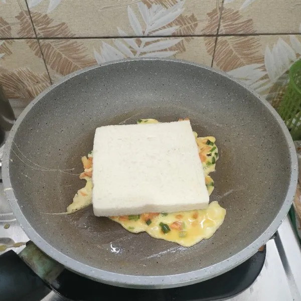 Taruh roti tawar diatas telur dadar, sambil ditekan pelan. Rapikan bagian tepinya.