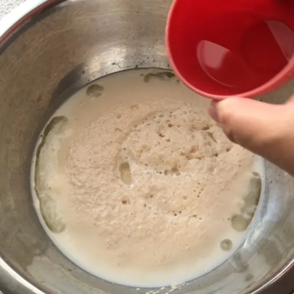 Dalam wadah, tuang susu hangat, gula pasir dan ragi, aduk dan biarkan hingga berbuih, lalu masukkan minyak goreng.