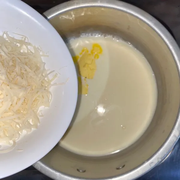 Masak susu cair dan kental manis sampai mendidih. Tambahkan margarin dan keju parut. Aduk sampai margarin larut.