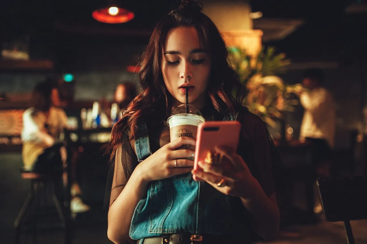 Anak perempuan sedang bermain ponsel saat minum kopi
