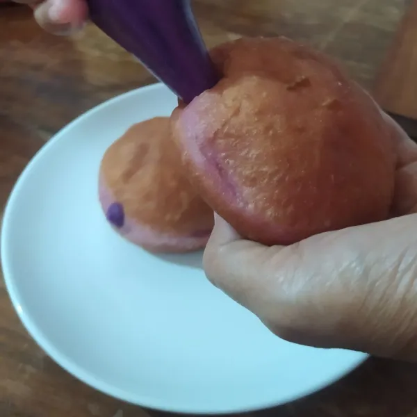 Tusuk pinggir bomboloni dengan sumpit. Semprotkan vla ubi ungu sampai penuh. Taburi dengan gula donat. Sajikan.