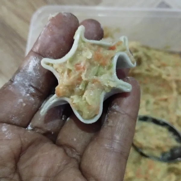 Ambil kulit gyoza, ambil sedikit adonan dimsum, ratakan. Putar dan rekatkan lalu beri topping wortel parut