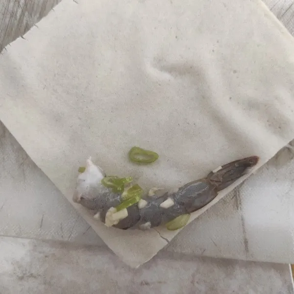 Ambil kulit lumpia lalu letakkan 1 udang beserta bawang putih dan daun bawang