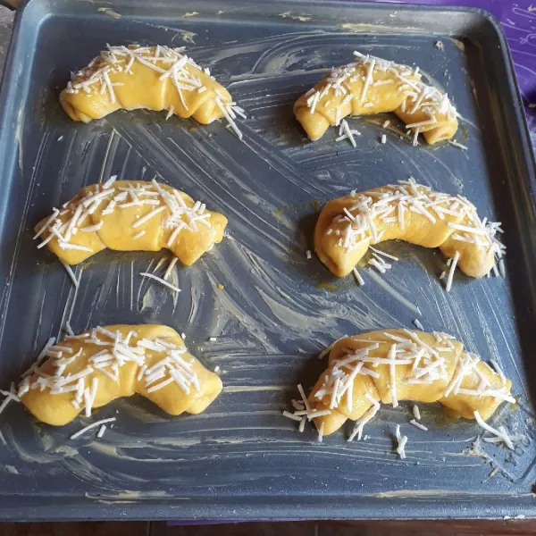 Olesi loyang dengan margarin. Letakkan roti di atas loyang dan lengkungkan. Diamkan 15 menit. Olesi atasnya dengan campuran bahan olesan, taburi keju.