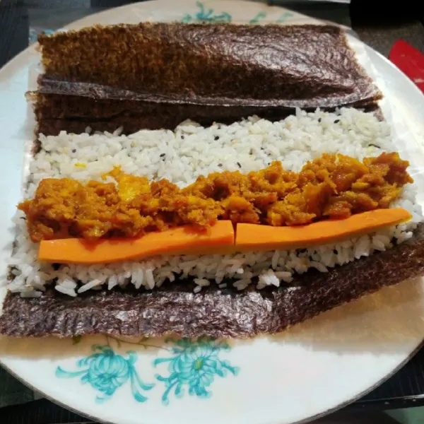 Siapkan selembar nori diatas plastik. Letakan nasi diatas nori. Tambahkan wortel, tuna suwir pedas. Lalu gulung nori sambil dipadatkan. Kemudian potong jadi 8 bagian