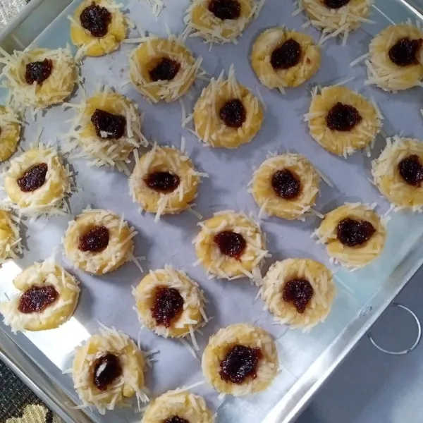 Tata di loyang yang telah diberi alas kertas roti. Tekan dengan jempol di tengahnya dan beri selai strawberry.