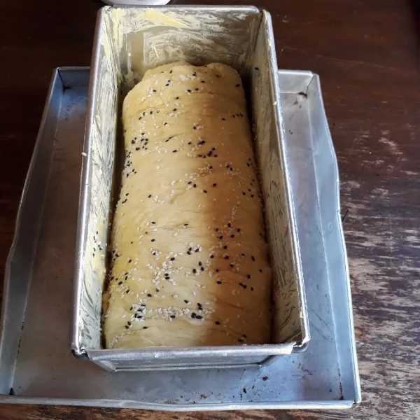 Gulingkan di atas wijen. Masukkan ke dalam loyang roti tawar 12 x 12 x 20 cm yang sudah diolesi margarin. Diamkan selama 25 menit.