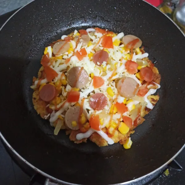 Panggang hingga bagian bawah sedikit kering, lalu balik. Beri saos barbeque, jagung, bawang bombay, sosis ayam, sosis sapi, keju cheddar, keju quick melt, tomat, mayonaise dan saos tomat. Tutup teflon lalu panggang