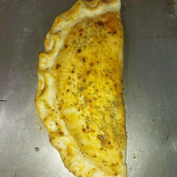 Oles permukaan calzone dengan saus bolognese, lalu taburi parsley bubuk, oven dengan suhu 170°c selama 15 menit.