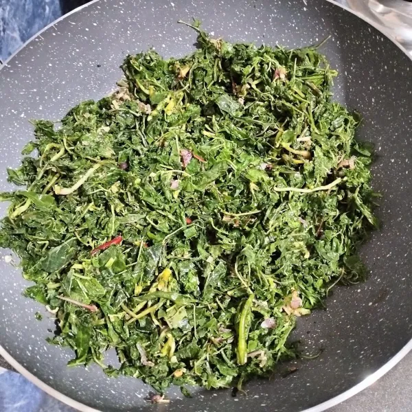 Masukkan daun singkong. Aduk sampai layu. Tuang air. Masak sampai air asat