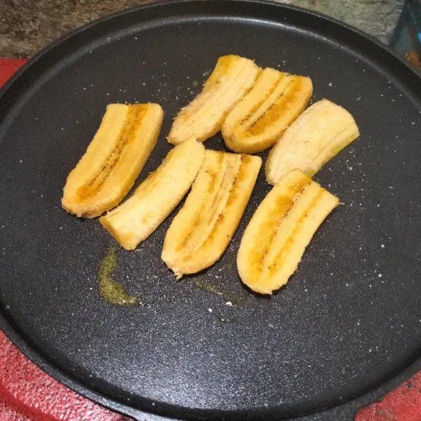Siapkan teflon, potong memanjang pisang menjadi beberapa bagian. Panggang pisang di atas teflon dengan mentega, lalu taburi sedikit gula untuk membuatnya semakin legit