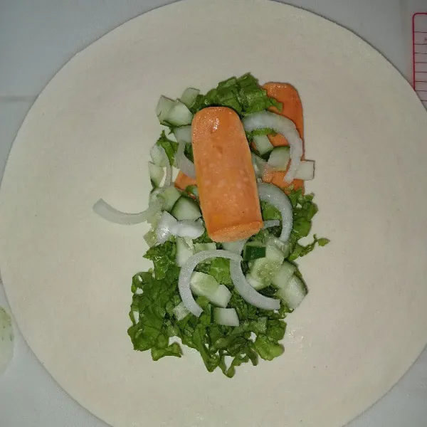 Siapkan kulit tortilla lalu letakkan sosis selada, mentimun dan bawang bombai