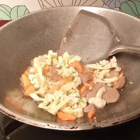 Tuang secukupnya air, masukkan bakso, wortel dan kembang kol. Aduk. Masak hingga sayuran setengah matang.