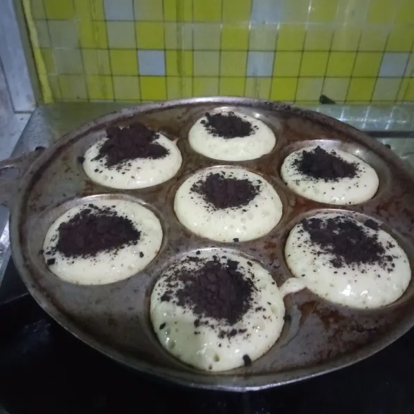 Proses hingga kue cubit mulai setengah matang atau mulai muncul lubang lubang di permukaannya. Taburi biskuit coklat crumble diatasnya lalu proses hingga kue cubit matang. Congkel kue cubit, lalu olesi kembali cetakan dengan margarin dan isi cetakan dengan adonan. Lakukan hingga adonan habis.