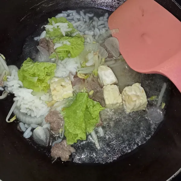 Masukkan nasi dan kaldu jamur, aduk rata masak hingga air sedikit menyusut.
