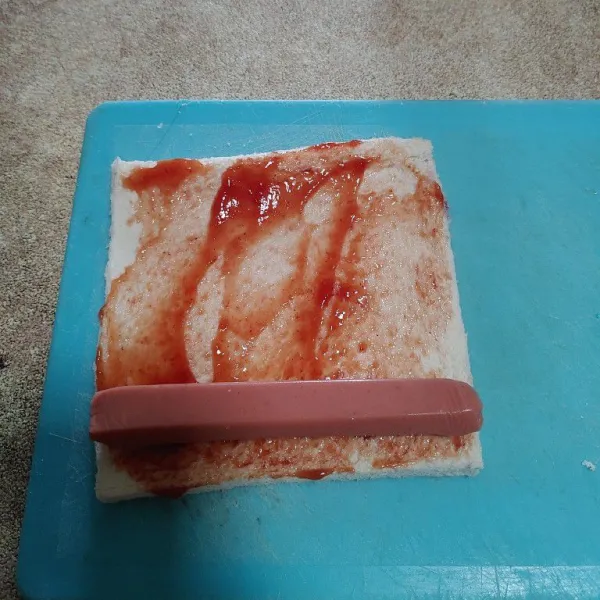 Tambahkan 1 sdm saos tomat, beri 1 buah sosis lalu gulung.