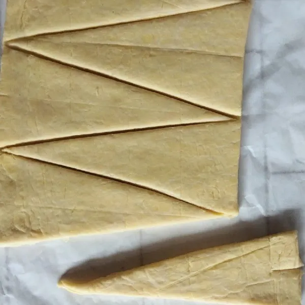 Kemudian pipihkan adonan berbentuk persegi panjang setebal 3 mm. Potong adonan 7-8 bentuk segitiga panjang. Gulung dan bentuk croissant seperti bulan sabit.