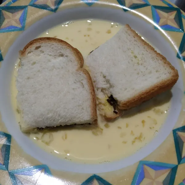 Lipat roti lalu belah jadi dua. Rendam roti di dalam kocokan telur dan susu, bolak balik.