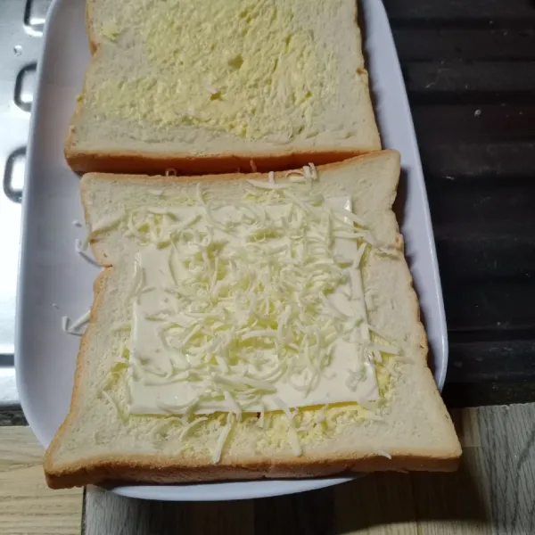 Letakkan 1 lembar keju slice dan keju parut pada 1 bagian roti.