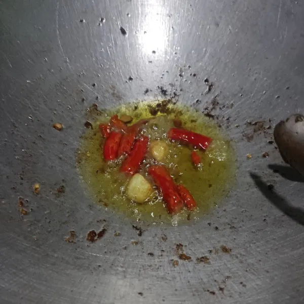 Goreng cabai dan bawang putih dalam minyak bekas menggoreng ayam hingga layu.
