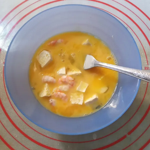 Kocok lepas telur bersama garam dan kaldu ayam bubuk. Tambahkan potongan tahu dan udang, aduk rata.