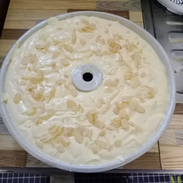 Tuang adonan ke loyang yang sudah dioles margarin dan ditabur tipis terigu. Hentakkan beberapa kali. Taburi toping almond.