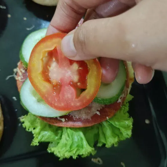 Beri tambahan selada, irisan timun, dan tomat, tutup dengan roti burger bagian atas, sajikan.