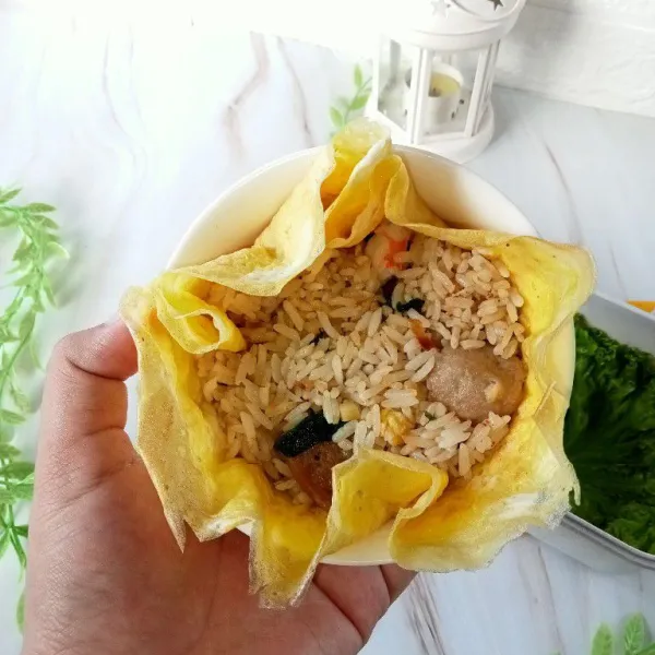 Ambil dadar telur, masukkan ke dalam mangkuk kemudian masukkan nasi goreng di atas telur lalu tutup rapat.