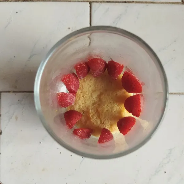 Siapkan wadah gelas, lalu masukkan sponge cake ke dalamnya. Tambahkan strawberry di atas cake, dengan cara menempelkan ke gelas kaca.