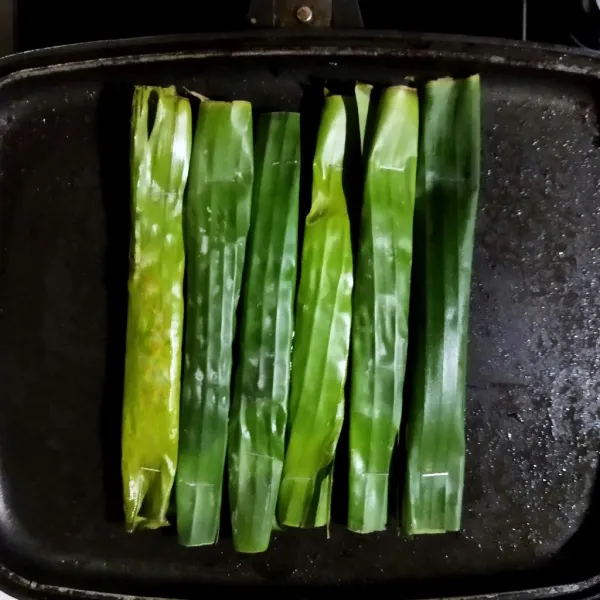 Bakar otak-otak yang sudah dikukus diatas teflon panas.