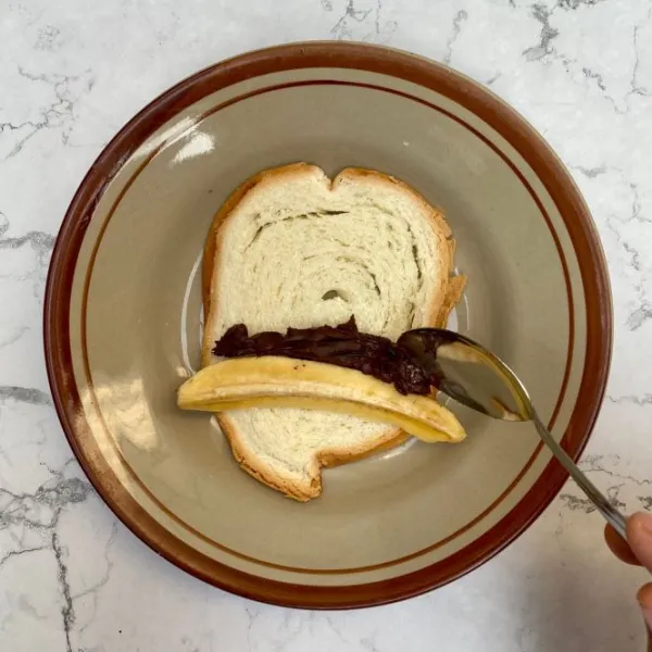 Tambahkan selai coklat, gulung lalu beri lem di ujung roti.