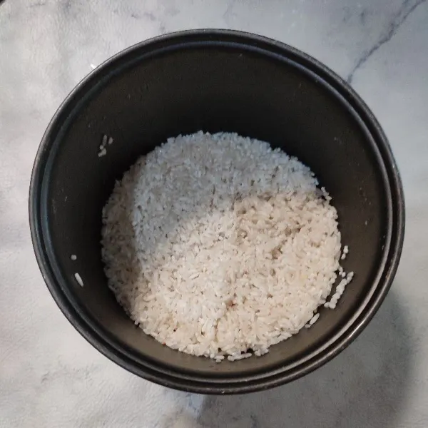 Cuci bersih beras, masukkan ke dalam panci rice cooker.