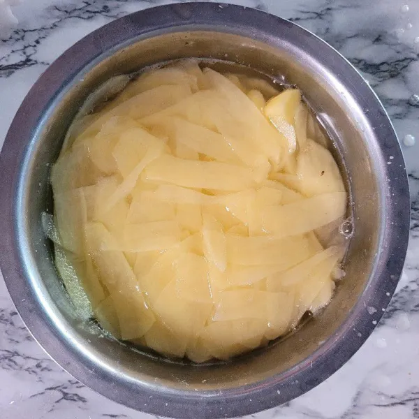 Cuci bersih kentang dan iris tipis, kemudian rendam di dalam air