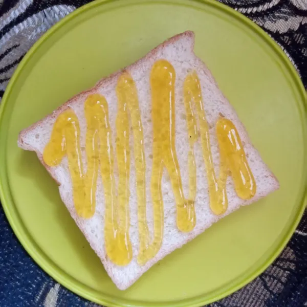 Siapkan selembar roti tawar, beri selai mangga.