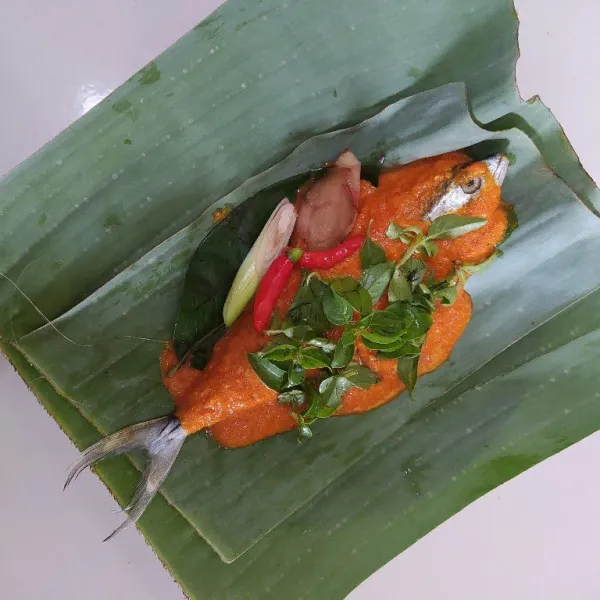 Ambil 1 lembar daun pisang lalu beri ikan yang telah dilumuri bumbu, tambahkan daun salam, daun jeruk, lengkuas, serai, cabe rawit dan daun kemangi.