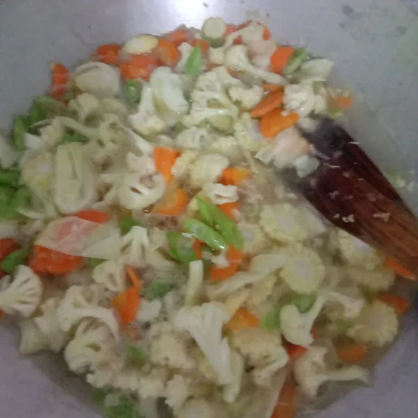 Lalu masukkan sayuran yang keras seperti bunga kol, kacang buncis, jagung kecil muda dan wortel, aduk sebentar lalu tambahkan air sambil diaduk, lalu tutup wajan dan diamkan selama 5 menit.