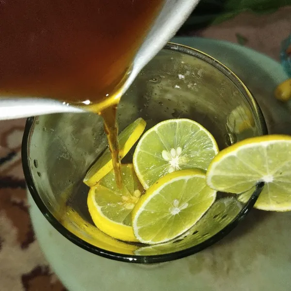 Dalam gelas, masukkan perasan jeruk nipis, irisan jeruk nipis, dan batu es. Kemudian tuang air teh hingga setengah gelas.