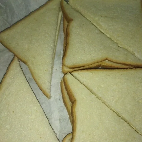 Lalu potong roti menjadi 2 bagian membentuk segitiga, tata roti di loyang yang sudah diberi alas baking paper.