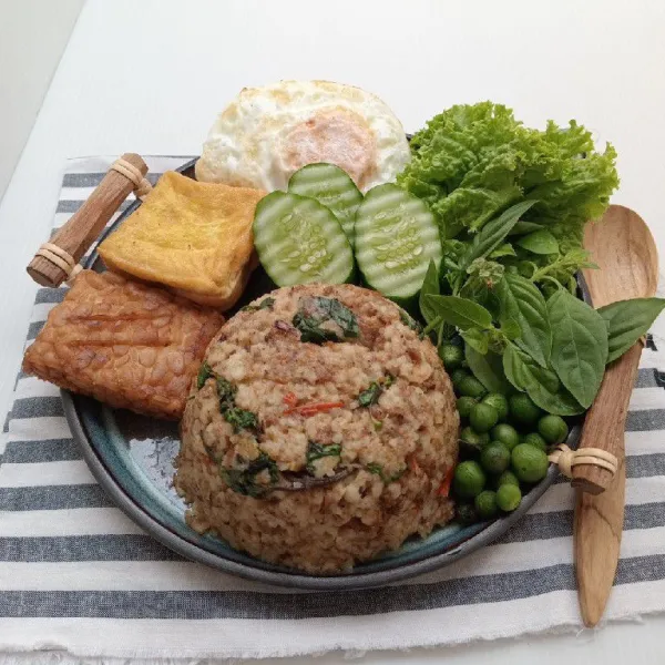 Sajikan nasi tutug oncom dengan tempe goreng, tahu goreng, telur goreng, timun, daun kemangi, leunca, dan daun selada bokor.