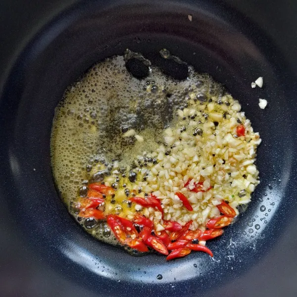 Masukkan cincangan bawang putih dan potongan cabai merah keriting. Masak hingga bawang putih kekuningan.