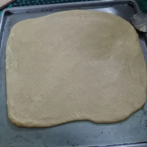 Setelah kalis bagi adonan menjadi 2 bagian, ambil 1 bagian adonan lalu gilas. Oles permukaannya dengan margarin.